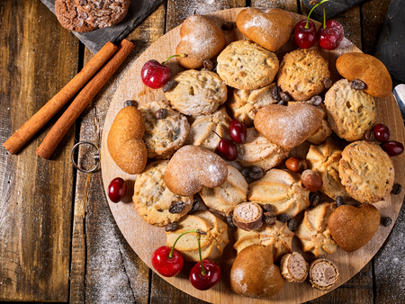 Oatmeal cookies and sand chocolate cake with cherry berry on cutting board on wooden table in rustic style. Top view of cinnamon stick still life.の写真素材