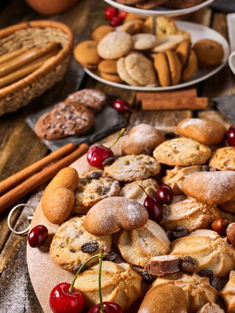 Oatmeal cookies and sand chocolate cake with cherry on cutting board on wooden table in rustic style served with cups and dessert spoons. Delight pleasant taste.の写真素材
