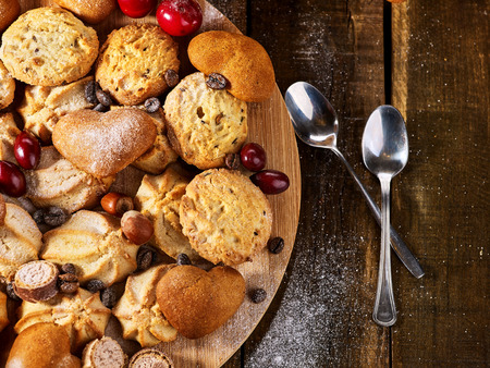 Oatmeal cookies and sand chocolate cake with cherry berry and crispy wafer rolls with cream on cutting board on wooden table in rustic style. Still life served with dessert spoons. Top view.の写真素材