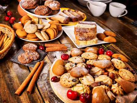 Oatmeal cookies and sand chocolate cake with cherry berry and crispy wafer rolls with cream on cutting board on wooden table in rustic style. Limitations for diabetics. Cherry in powdered sugar.の写真素材