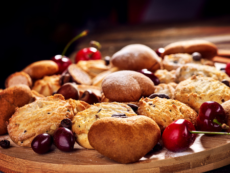 Oatmeal cookies and sand chocolate cake with cherry berry and crispy wafer rolls with cream on cutting board on wooden table in rustic style. Supplement for breakfast.の写真素材