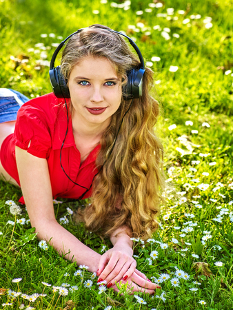 Girl in headphones catch rhythm music on green grass with chamomile flowers summer outdoor. Walking increases duration of sleep.の写真素材