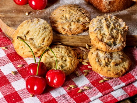 Oatmeal cookies with husk oats and cherry on kitchen cutting board gingham checkered cotton fabric on table in village style for picnic close up. Added powdered sugar. Professional recipes.の写真素材