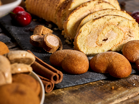Sand cookies heart shape, rolled cake with cherry and cinnamon stick, coffee bean on kitchen on wooden table in village style. Increase performance and mood.の写真素材