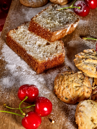 Baking homemade cake. Oatmeal cookies with husk oats and cherry cupcake with powdered sugar on kitchen cutting board gingham checkered cotton fabric on table in village style for picnic.の写真素材
