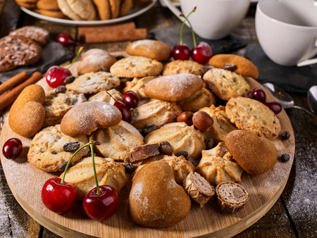 Oatmeal cookies and sand chocolate cake with cherry berry on cutting board on wooden table in rustic style. Cups and dessert spoons. Easily digestible and quickly digestible substances.の写真素材