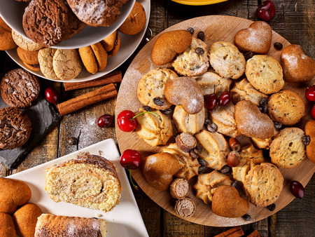 Oatmeal cookies and sand chocolate cake with cherry berry and crispy wafer rolls with cream on cutting board on wooden table in rustic style. Useful for digestion.の写真素材
