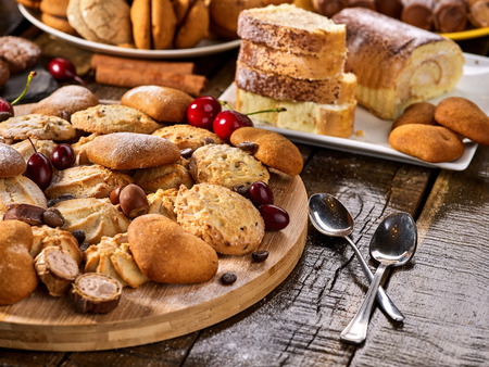Oatmeal cookies and sand chocolate cake with cherry berry and crispy wafer rolls with cream on cutting board on wooden table in rustic style. Still life served with dessert spoons. Traditional dish.の写真素材