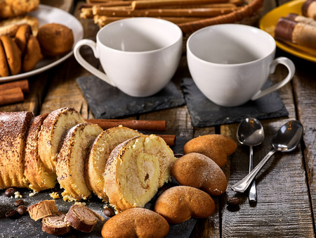 Sand cookies heart shape, rolled cake with cherry and cinnamon stick, coffee cups on kitchen on wooden table in village style. Useful for digestion. Problems with excess weight.の写真素材