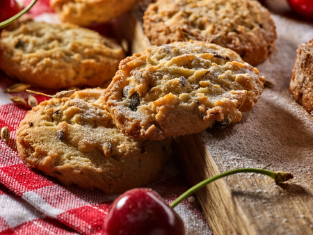 Oatmeal cookies with husk oats and cherry on kitchen cutting board gingham checkered cotton fabric on table in village style for picnic close up. Culinary products to order.の写真素材