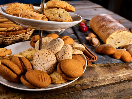 Oatmeal and nut cookies and sand biscuit on tier cake stand with straw pastry in basket on kitchen on wooden table in rustic natural style. Top view of two cups of tea on wooden table. Perfect productの写真素材
