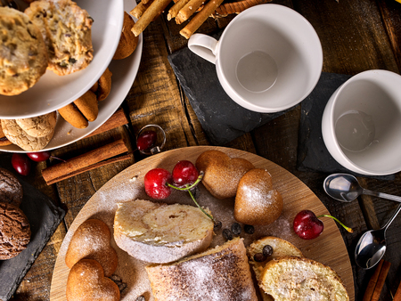 Sand nut chocolate cookies and rolled biscuit on board and cinnamon stick. Straw pastry with cup of coffee with dessert spoonon on wood kitchen table in rustic style. Served hot.の写真素材