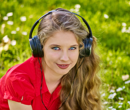 Girl in headphones catch rhythm music on green grass with chamomile flowers summer outdoor. Closeup portrait.の写真素材