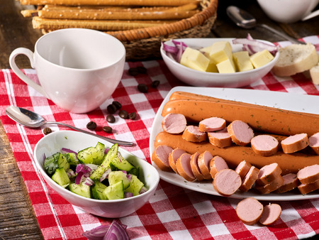 Sausage portion with bread baguette on table setting on checkered tablecloth and cup in farm style. Lunch in inexpensive cafe.の写真素材