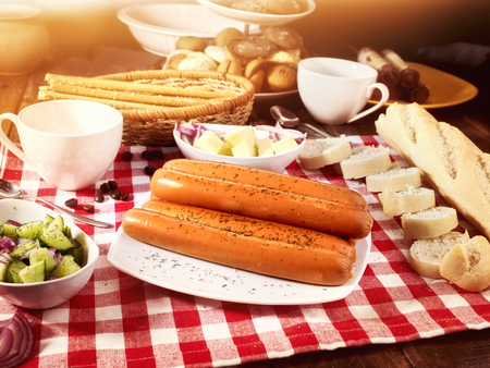 Sausage portion with bread baguette on table setting on checkered tablecloth and cup in farm style.の写真素材