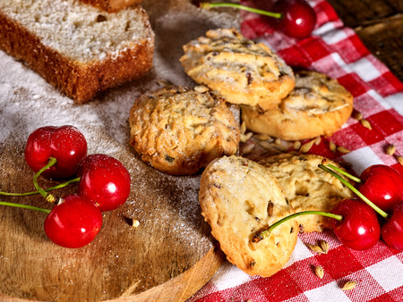 Oatmeal cookies with husk oats and cherry cupcake with powdered sugar on kitchen cutting board gingham checkered cotton fabric on table in village style for picnic. Delicious, homemade cupcake.の写真素材