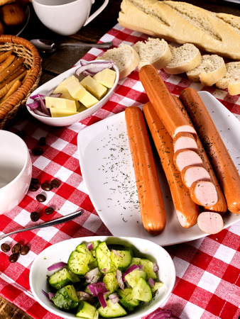 Sausage portion with bread baguette on table setting on checkered tablecloth and cup in farm style. Composition of meat products.の写真素材