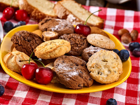 Chocolate oatmeal cookies and sand heart shape cake with blueberries on table in farm style. Table setting breakfast on gingham tablecloth.の写真素材