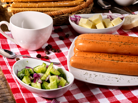 Sausage portion with bread baguette on table setting on checkered tablecloth and cup in farm style. Soy products.の写真素材