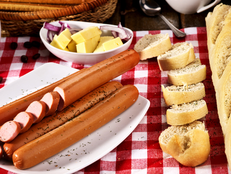 Sausage portion with bread baguette on table setting on checkered tablecloth and cup in farm style. Cozy, homely atmosphere.の写真素材