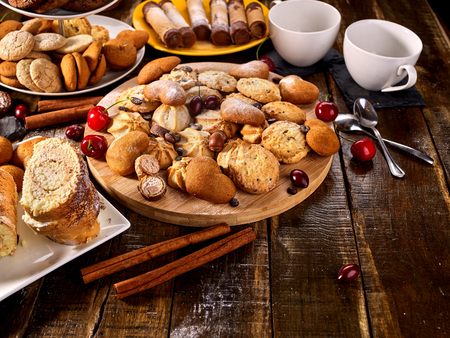 Oatmeal cookies and sand chocolate cake with cherry berry and crispy wafer rolls with cream on cutting board on wooden table in rustic style. Delight pleasant taste.の写真素材