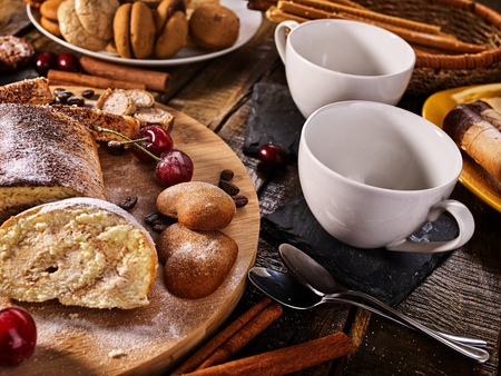 Rolled biscuit and sand chocolate cookies on board. Cinnamon stick and cherry on kitchen wood table in rustic style. Cooking various dishes.の写真素材