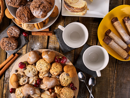 Oatmeal cookies and sand chocolate cake with cherry berry on cutting board on wooden table in rustic style. Top view of still life served with cups and dessert spoons. Increase performance and mood.の写真素材