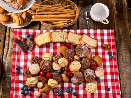 Cookies biscuit with blueberry. Chocolate bake and cherry cupcake with cup tea or coffee and tier stand on kitchen gingham checkered cotton fabric on wooden table village style for picnic top view.の写真素材
