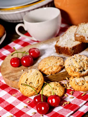 Oatmeal cookies and cherry on kitchen cutting board gingham checkered cotton fabric on table in village style for picnic. Cooking technology. Culinary courses.の写真素材