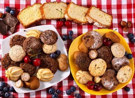Oatmeal Cookies and sand chocolate cake with blueberries on wooden table with gingham cloth in farm style close up. Table setting breakfast for two with cups in. Beautiful table setting.の写真素材