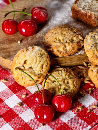 Oatmeal cookies with husk oats and cherry on kitchen cutting board gingham checkered cotton fabric on table in village style for picnic close up. Breakfast for loved one.の写真素材