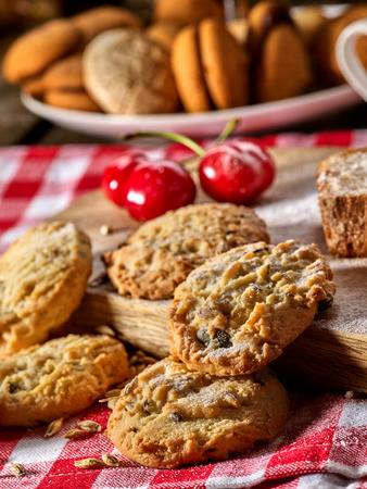 Oatmeal cookies and cherry on kitchen cutting board gingham checkered cotton fabric on table in village style for picnic with plate of macaron background. Exhibition of culinary works.の写真素材