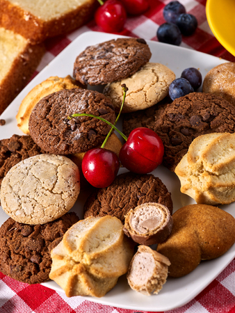 Chocolate oatmeal cookies and sand heart shape cake with blueberries on table in farm style. Table setting breakfast on gingham tablecloth. Homemade, delicious recipes.の写真素材