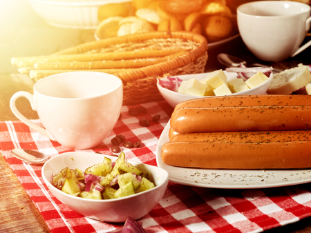 Sausage portion with bread baguette on table setting on checkered tablecloth and cup in farm style. Soy products. Serve this dish hot. Soft, beautiful, sunshine.の写真素材