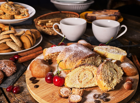 Sand nut chocolate cookies and rolled biscuit on board and cinnamon stick and straw pastry on kitchen on wood table in rustic style top view. Cups of tea and dessert spoon. Eat in small portions.の写真素材