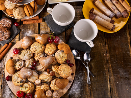 Oatmeal cookies and sand chocolate cake with cherry berry on cutting board on wooden table in rustic style. Top view of still life served with cups and dessert spoons. Perfect for breakfast.の写真素材