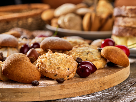 Oatmeal cookies and sand chocolate cake with cherry berry and crispy wafer rolls with cream on cutting board on wooden table in rustic style. Eat this dish can be both hot and cold.の写真素材