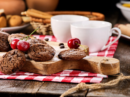 Oatmeal chocolate cookies with coffee grains and cherry, powdered sugar on kitchen cutting board with checkered fabric on wooden table in village style for picnic. Preservation of sugar balance.の写真素材