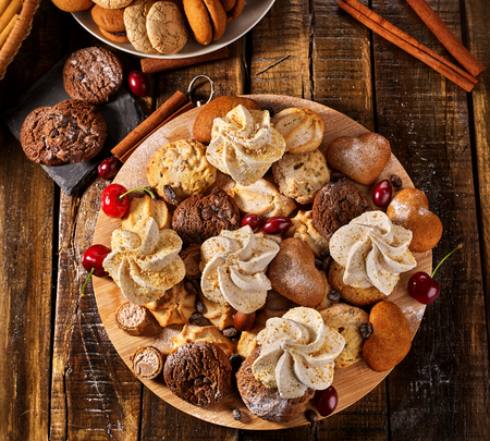 Oatmeal cookies and sand chocolate cake with cherry berry and crispy wafer rolls with cream on cutting board on wooden table in rustic style. Limitations for diabetics. Yummy.の写真素材