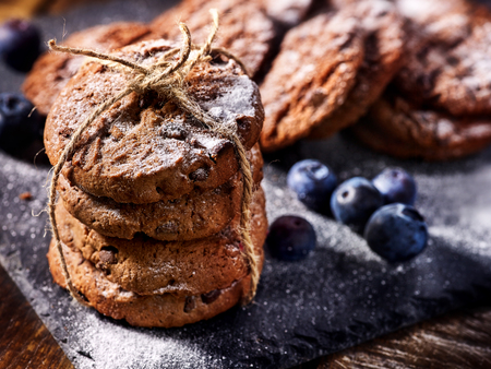 Serving food on slate onto wooden table. Oatmeal cookies biscuit with blueberry on picnic dark tiles countrylike. Chocolate chip cookies tied with string. Best range of confectionery products.の写真素材
