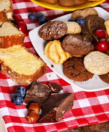 Oatmeal Cookies and sand chocolate cake with blueberries on wooden table with gingham cloth in farm style close up. Table setting breakfast for two with cups in. How and from what make sweets.の写真素材