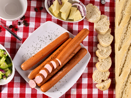 Sausage portion with bread baguette on table setting on checkered tablecloth and cup in farm style. Composition of meat products. Chemical-free meat products.の写真素材