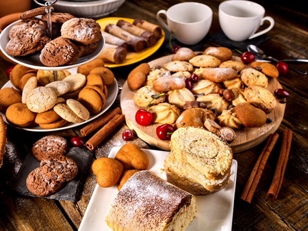 Oatmeal cookies and sand chocolate cake with cherry berry and crispy wafer rolls with cream on cutting board on wooden table in rustic style. Limitations for diabetics. There is no monotony in food.の写真素材
