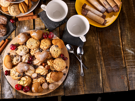 Oatmeal cookies and sand chocolate cake with cherry berry on cutting board on wooden table in rustic style. Top view of still life served with cups and dessert spoons. Useful for digestion.の写真素材