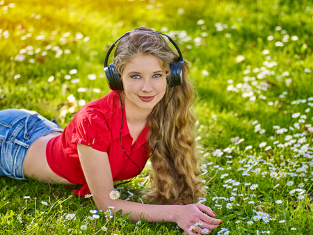 Girl in headphones catch rhythm music on green grass with chamomile flowers summer outdoor. Walking strengthen the immune system.の写真素材
