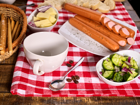 Sausage portion with bread baguette on table setting on checkered tablecloth and cup in farm style. Chemical-free meat products.の写真素材