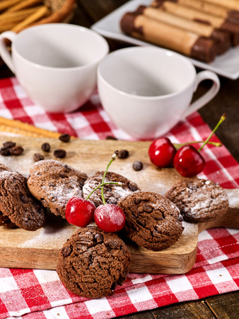 Oatmeal chocolate cookies with coffee grains and cherry, powdered sugar on kitchen cutting board with checkered fabric in village style for picnic. Macaron in background. Useful for digestion.の写真素材