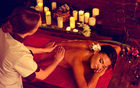 Masseuse give massage to woman in spa salon with light candles .の写真素材