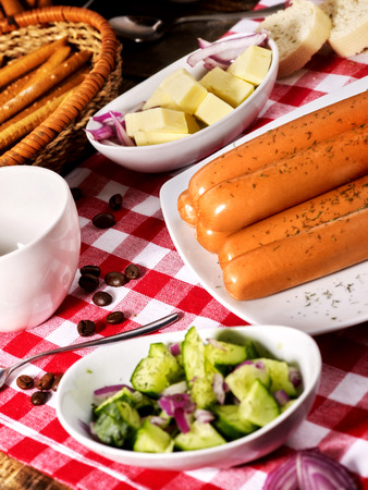 Sausage portion with bread baguette on table setting on checkered tablecloth and cup in farm style. High protein content.の写真素材