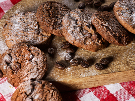 Oatmeal chocolate cookies with coffee grains, powdered sugar on kitchen cutting board with checkered fabric on wooden table in village style for picnic. Rejection of many products.の写真素材